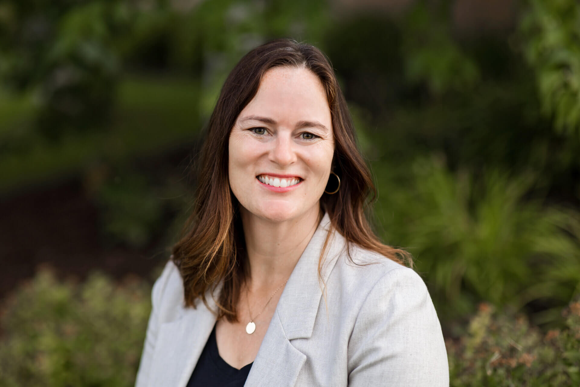 Dana Anderson has collarbone length brown hair. She is wearing a light gray blazer and is smiling.