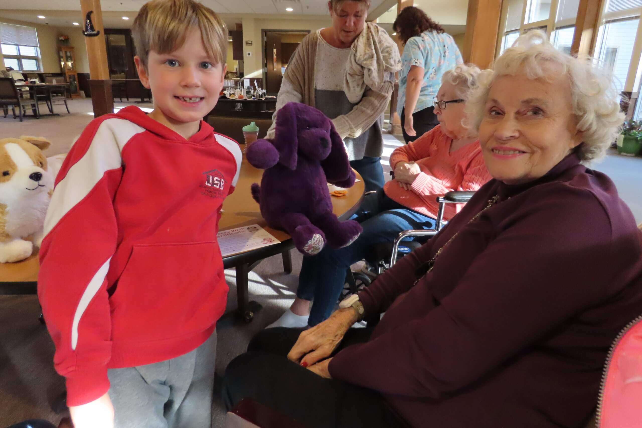 A young boy in a red sweatshirt stands next to an older woman in a purple sweater. They are both smiling.