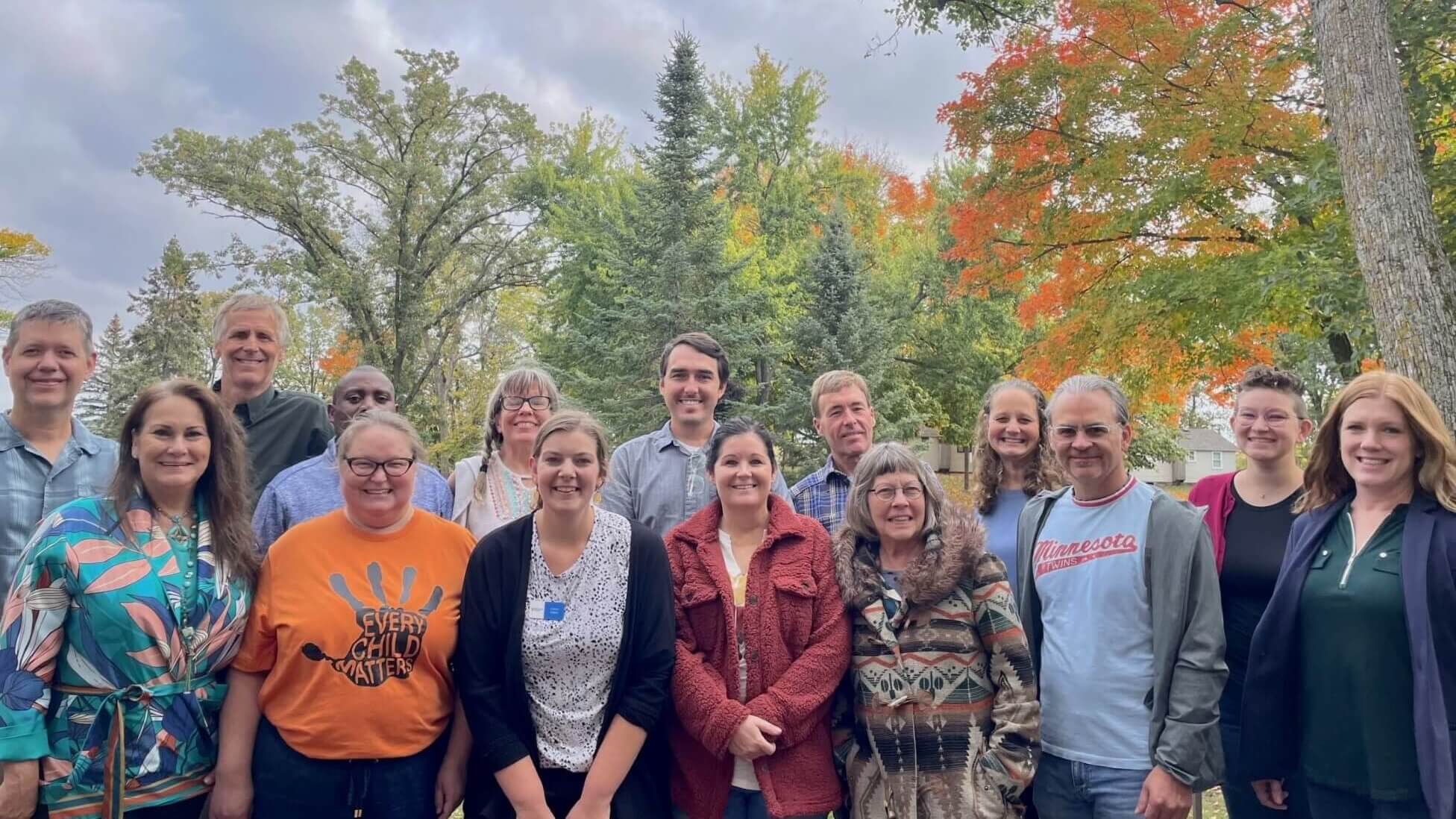 The cohort group is made up of 15 people standing outside in autumn.