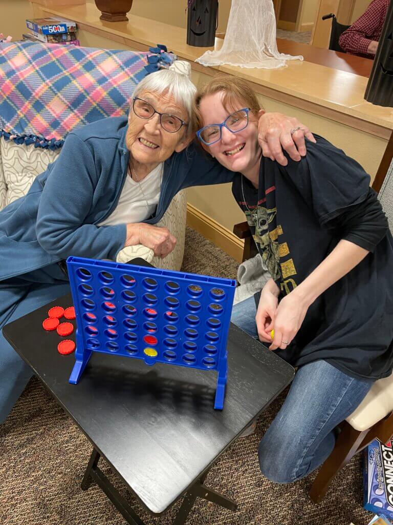 An older woman and a child hug and smile while playing connect four.