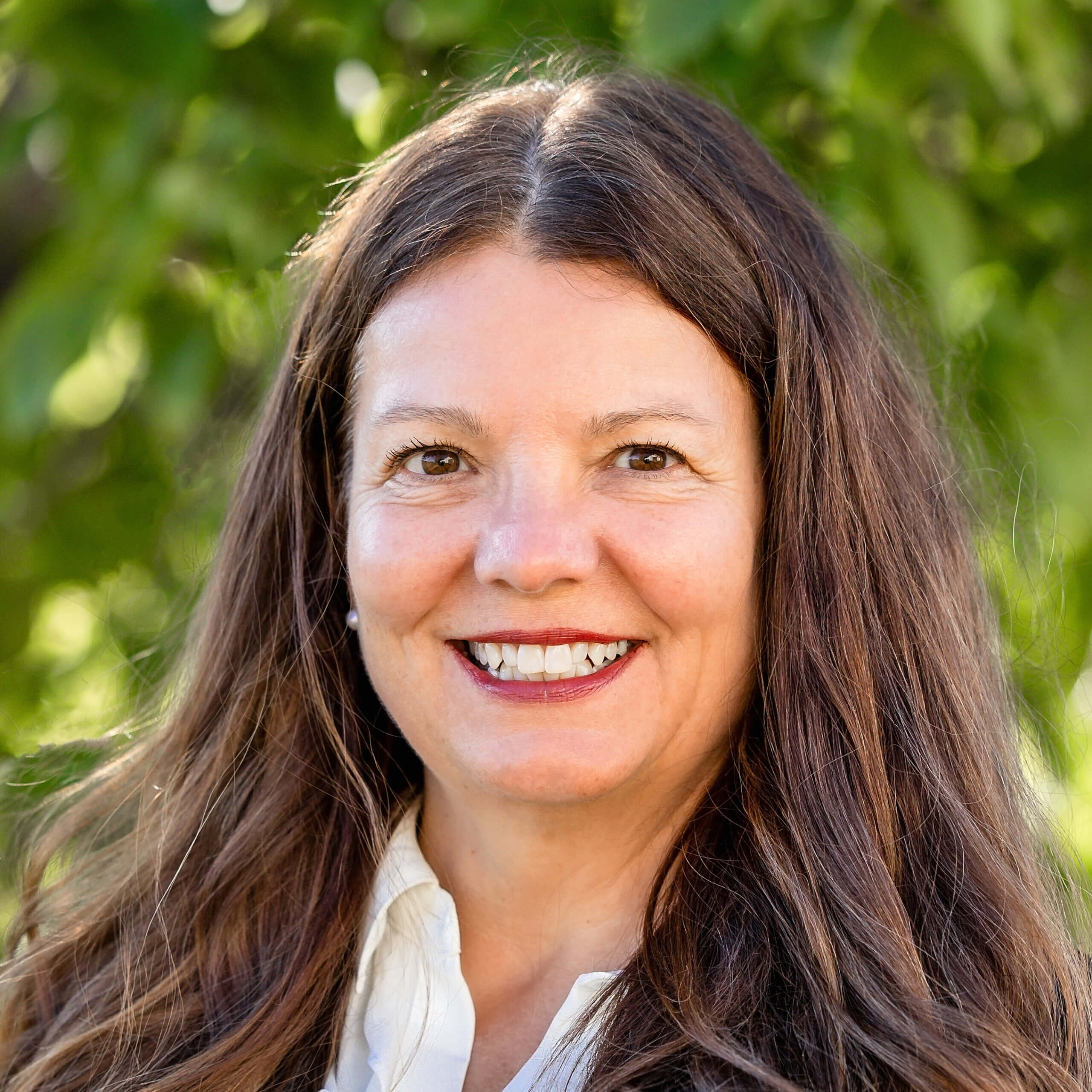 Camille Pearson Walz is smiling outdoors in front of a green tree.