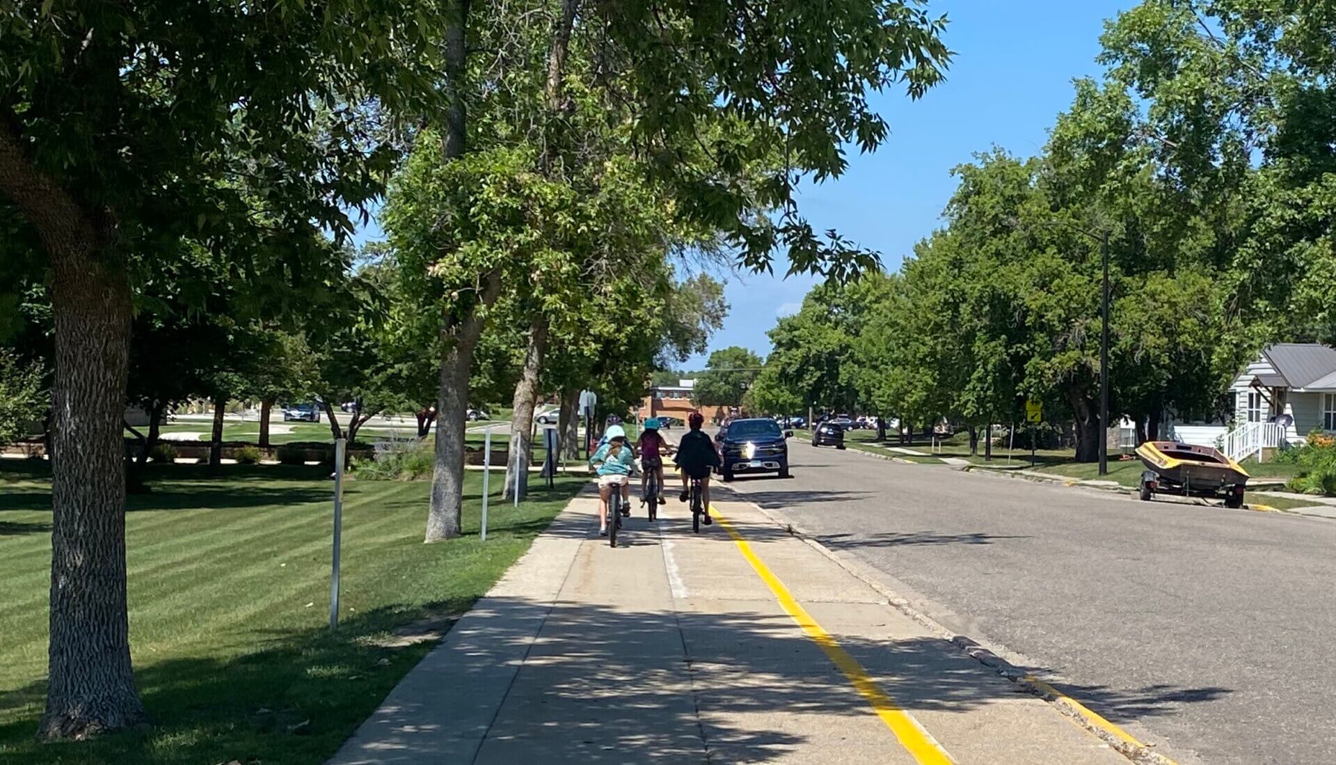 Kids riding bikes on the side walk to school on a sunny day.