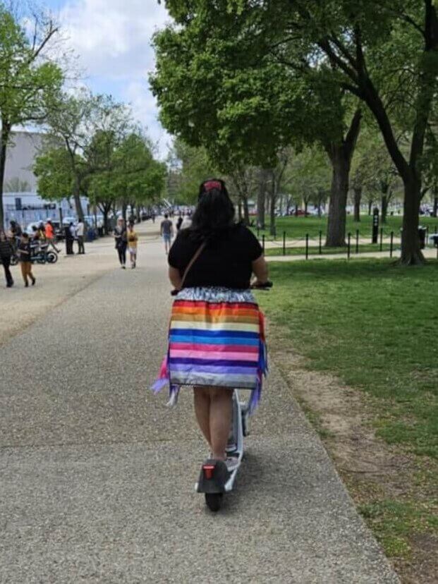 Bunker riding a scooter in her ribbon skirt.