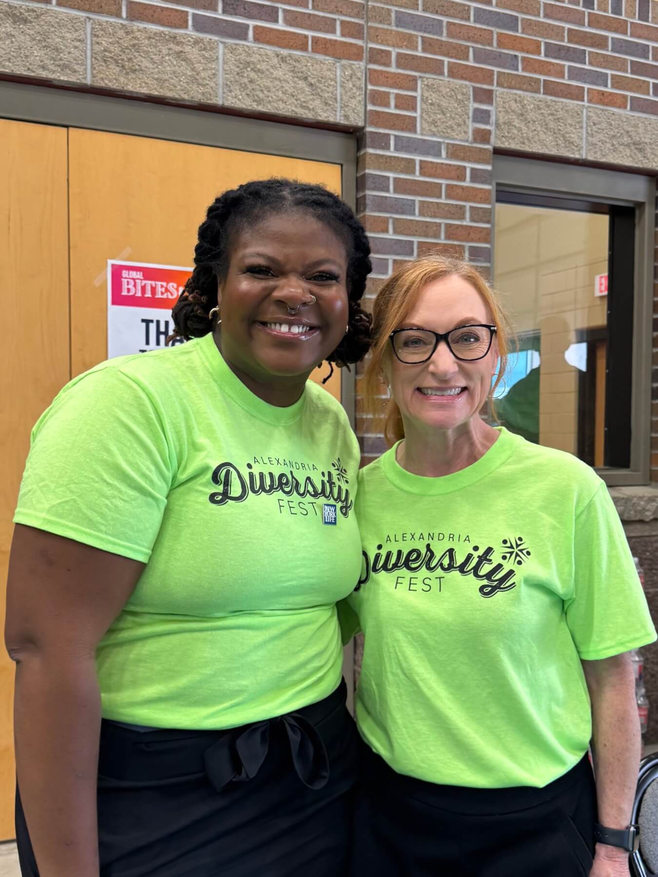 Simi and another volunteer smile at the camera in bright green shirts.