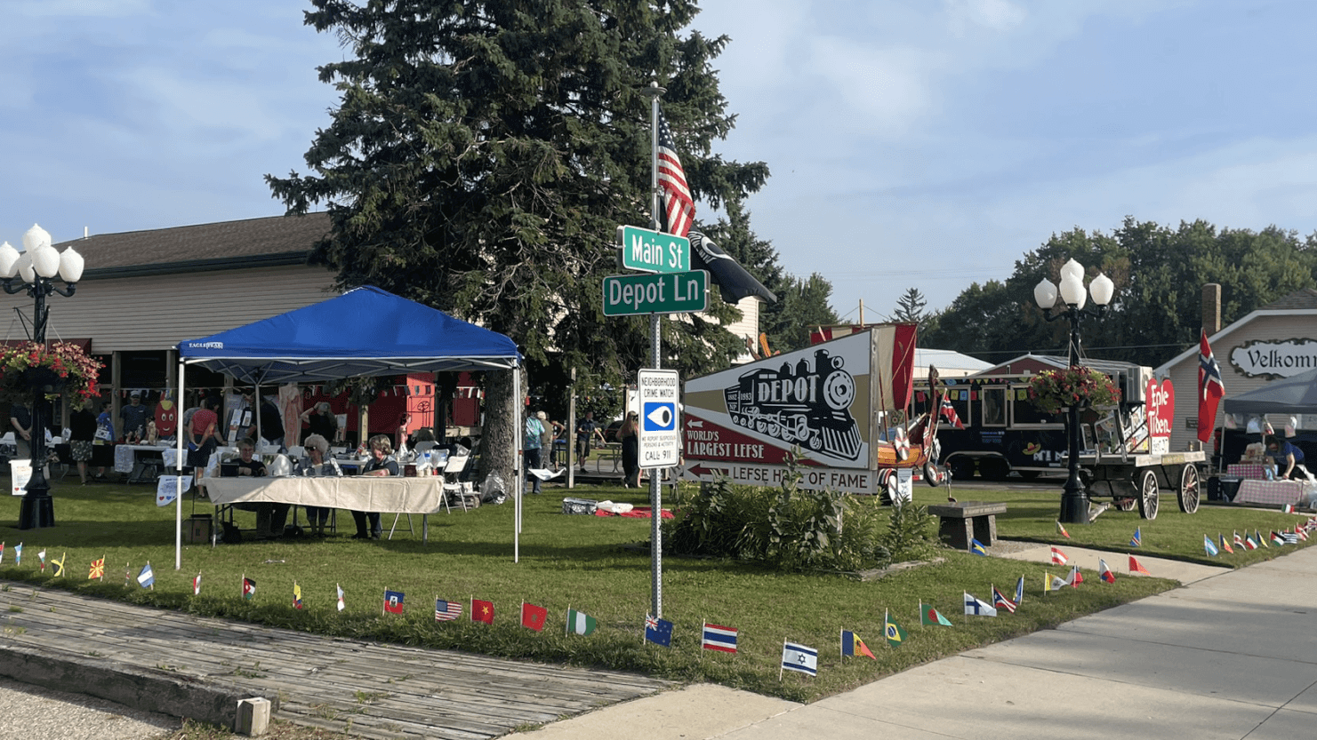 The front of the Starbuck Depot. There are tents on the green grass. There are small flags around the border of the lawn.